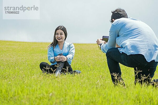 Ein Mann fotografiert ein Mädchen auf dem Feld  Ein Freund fotografiert seine Freundin auf dem Feld  Zwei Freunde fotografieren mit dem Handy auf dem Feld