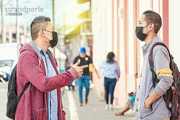 Zwei junge Leute mit Maske unterhalten sich im Freien  zwei Freunde mit Gesichtsmaske unterhalten sich  Konzept des Gesprächs und der sozialen Distanz