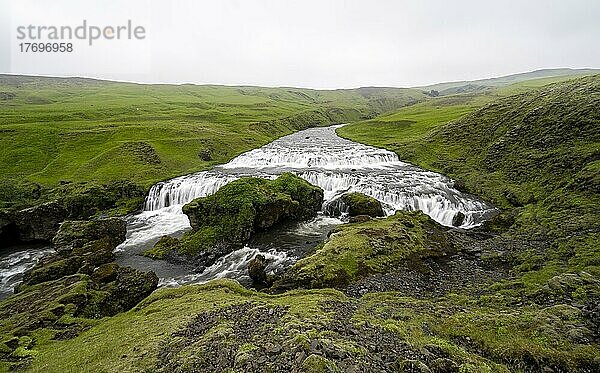 Breiter Wasserfall zwischen grünen Wiesen  Steinbogafoss  Landschaft am Fimmvörðuháls Wanderweg  Südisland  Island  Europa