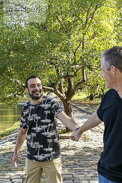 Ein schwuler Mann ist überrascht und glücklich  weil sein Freund in der Öffentlichkeit seine Hand hält  während sie an einem See spazieren gehen. Coming-out-Konzept