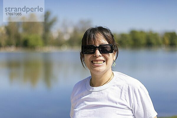 Porträt einer jungen lateinischen Frau  die lächelnd in die Kamera schaut  an einem See mit Kopierraum