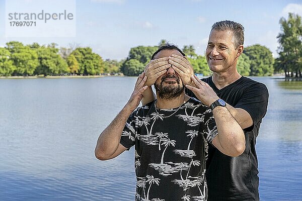 Ein Paar reifer schwuler Männer  von denen der eine den anderen überrascht  indem er seine Augen in einem See verdeckt. Konzept der Überraschung  Glück  Spiel