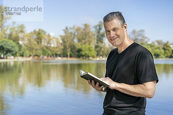 Älterer Mann  der an einem See liest und die freie Zeit an einem sonnigen Tag genießt
