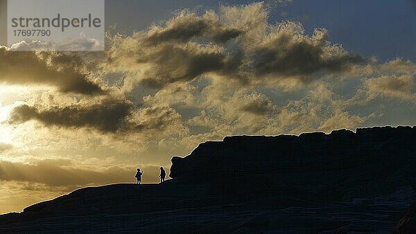 Morgenlicht  Gegenlicht  2 Menschen als Silhouetten  grau-weiße Wolken  Tuffgestein  Tuff-Felsen  Sarakiniko Beach  Insel Milos  Kykladen  Griechenland  Europa