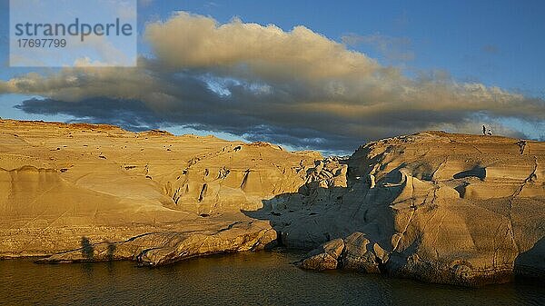 Morgenlicht  blauer Himmel  grau-weiße Wolken  vom Morgenlicht angestrahltes Tuffgestein  2 Menschen auf Tuff-Felsen  Meeresarm  Sarakiniko Beach  Insel Milos  Kykladen  Griechenland  Europa