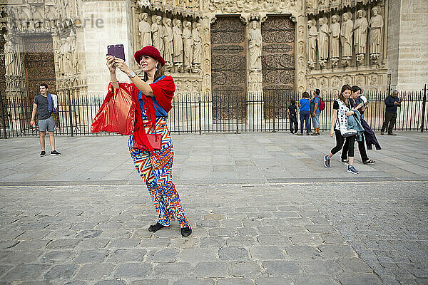 Eine Frau in farbenfroher Kleidung macht ein Selbstporträt vor der Kathedrale Notre Dame in Paris  Frankreich; Paris  Frankreich