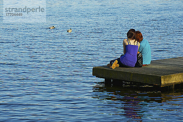 Ein junges Paar kuschelt zusammen auf einem hölzernen Dock entlang des Flusses; Hamburg  Deutschland