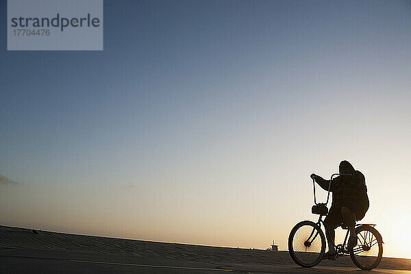 Silhouette eines Radfahrers  der auf der Promenade neben dem Strand bei Sonnenuntergang fährt; Kalifornien  Vereinigte Staaten von Amerika