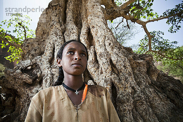 Porträt eines jungen Mädchens  das vor einem großen Baum steht; Äthiopien