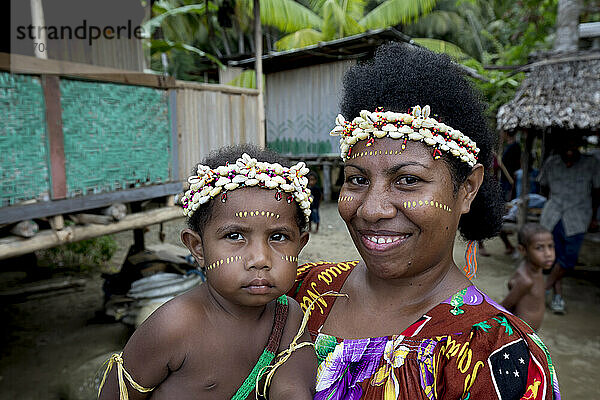 Mutter und Kind mit Muschel-Stirnbändern am Ufer des Dorfes Siboma  Insel Lababia  Huon-Golf  Provinz Morobe  Papua-Neuguinea; Dorf Siboma  Provinz Morobe  Papua-Neuguinea