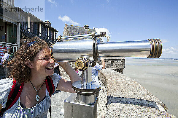 Junge Frau  die durch ein Teleskop auf den Mauern des Mont Saint Michel schaut  Normandie  Frankreich