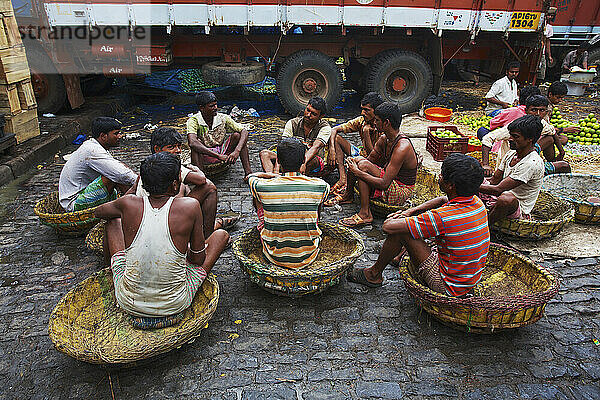 Junge Männer sitzen in Körben und unterhalten sich auf dem Obstmarkt; Kolkata  Indien