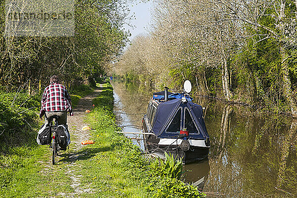 Radfahrer  der entlang des Kanals radelt und ein Schmalspurboot passiert; Wiltshire  England