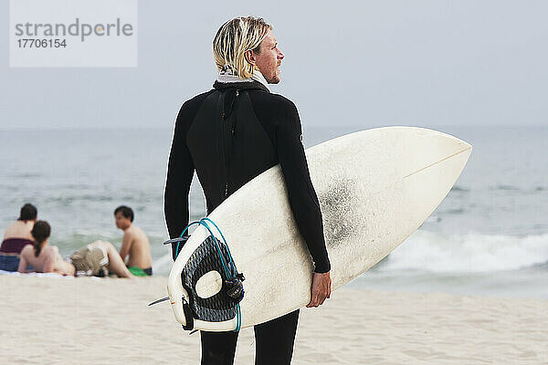 Ein Surfer steht am Strand  hält sein Surfbrett und schaut auf das Wasser hinaus; Kalifornien  Vereinigte Staaten von Amerika