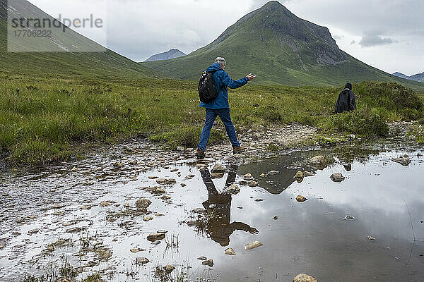 Ein Wanderer überquert einen kleinen Bach entlang eines Weges in den Cuillin Mountains in der Nähe von Sligachan; Isle of Skye  Schottland