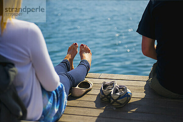 Zwei Menschen sitzen auf einem hölzernen Dock am Rande des Wassers; Barcelona  Spanien