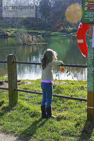 Ein junges Mädchen steht an einem Zaun und blickt auf einen ruhigen See  Hamstead Heath; London  England