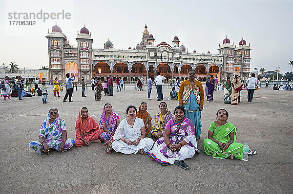 Eine Gruppe von Frauen in bunten Saris sitzen zusammen auf dem Boden mit dem Mysore-Palast im Hintergrund; Mysore  Indien