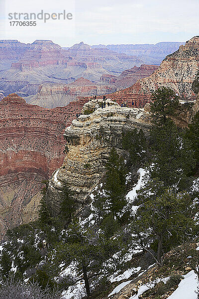 Weitwinkel-Vertikalaufnahme des Grand Canyon im Winter mit Touristen  die sich unterhalten und auf einem Felsvorsprung fotografieren; Arizona  Vereinigte Staaten von Amerika