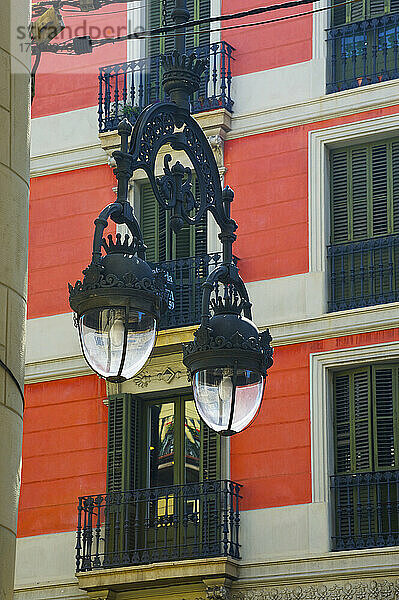 Eine verschnörkelte Metallleuchte vor einem roten Wohnhaus; Barcelona  Spanien