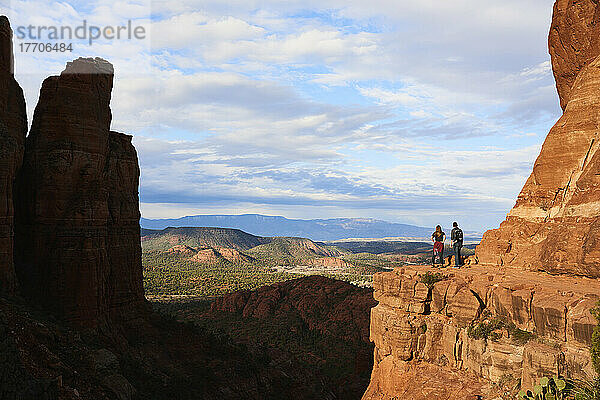 Zwei junge Wanderer stehen auf einem roten Felsvorsprung und genießen den weiten Blick auf die Sedona-Schlucht und die fernen Berge; Sedona  Arizona  Vereinigte Staaten von Amerika