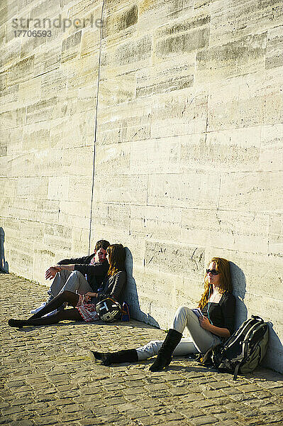 Junge Menschen  die an einer Mauer in der Sonne sitzen; Paris  Frankreich