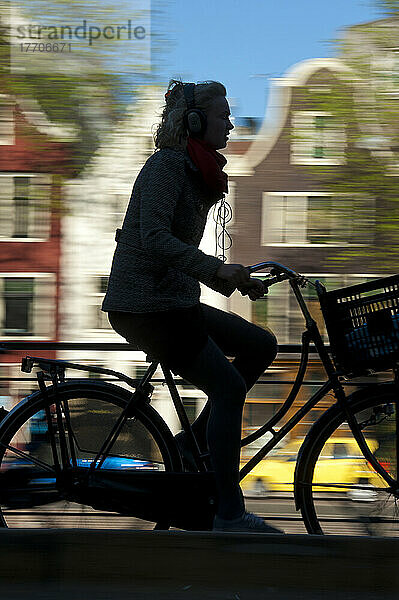 Silhouette eines Radfahrers  der an einer Gracht und Giebelhäusern vorbeifährt; Amsterdam  Holland