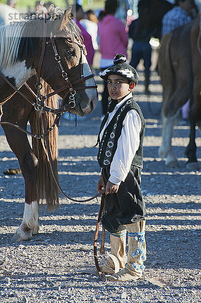Ein Junge in traditioneller Tracht steht neben einem Pferd; Malargue  Argentinien