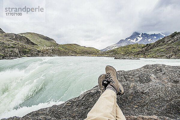 Sitzen auf einem Felsen mit Blick auf einen rauschenden Bergfluss; Tores Del Paine  Magallanes  Chile