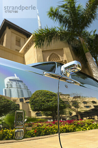 Detail eines verchromten Rolls Royce unter einer Palme und einem traditionellen Hotel im arabischen Stil mit dem Burj Khalifa dahinter; Dubai  Vereinigte Arabische Emirate