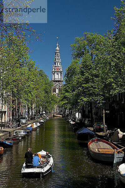 Menschen in einem kleinen Boot  das einen kleinen Kanal entlangfährt  mit der Spitze der Zuiderkerk-Kirche dahinter; Amsterdam  Holland