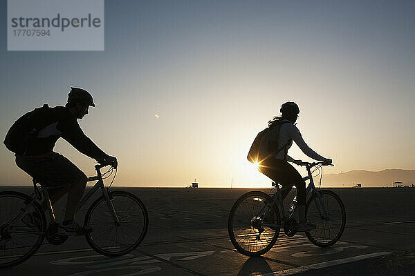 Silhouette von Radfahrern  die auf der Promenade neben dem Strand bei Sonnenuntergang fahren; Kalifornien  Vereinigte Staaten von Amerika