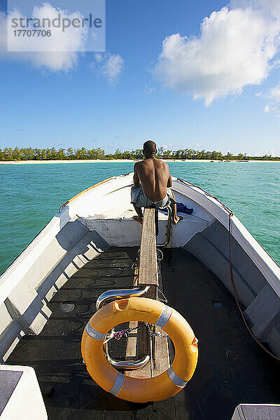 Ein Mann sitzt auf seinem Boot auf dem ruhigen türkisfarbenen Indischen Ozean mit Blick auf den weißen Sandstrand; Vamizi Island  Mosambik