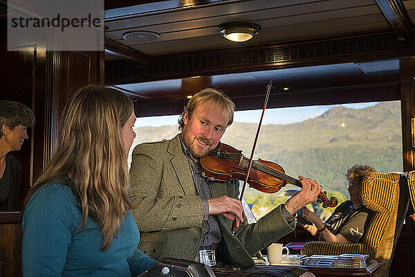 Ein Geiger spielt für Gäste an Bord eines Bootes; Kyle of Lochalsh  Schottland