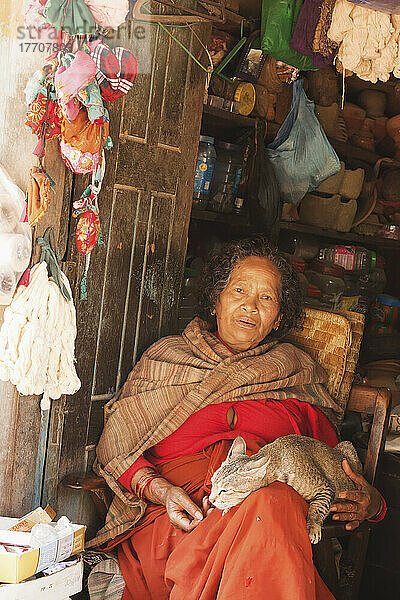 Alte Newar-Frau in traditioneller Kleidung hält ihre Katze in der Eingangstür ihres Ladens; Bhaktapur  Nepal