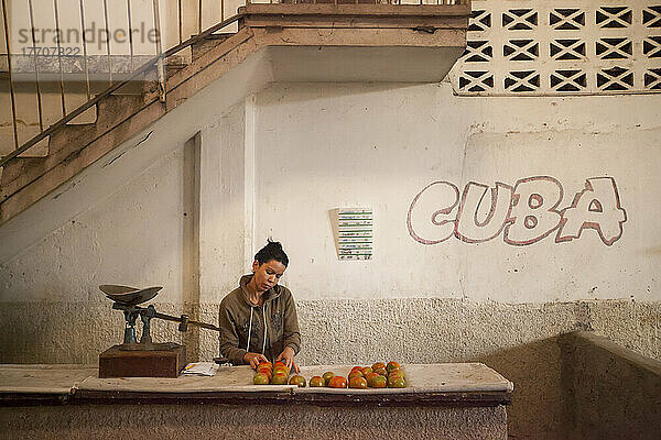 Eine Frau kümmert sich um Äpfel an einem Stand auf einem Bauernmarkt mit kubanischem Graffiti an der Wand; Cienfuegos  Kuba.