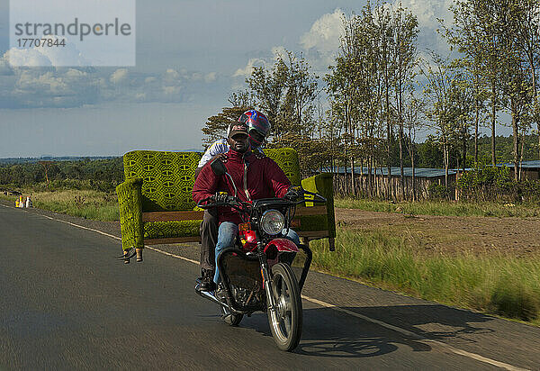 Zwei Männer auf einem Motorrad tragen ein Sofa auf dem Rücken auf der Straße  in der Nähe von Nanyuki; Kenia