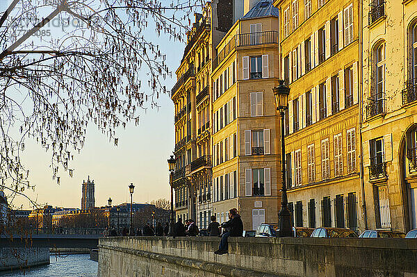 Ein Paar sitzt zusammen auf einer Kanalmauer mit Sonnenuntergang Sonnenlicht auf die Gebäude gegossen; Paris  Frankreich