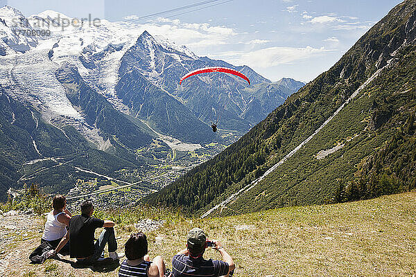 Touristen  die einen Gleitschirmflug am Startplatz über dem Chamonix-Mont-Blanc-Tal beobachten  mit dem Mont Blanc im Hintergrund; Frankreich