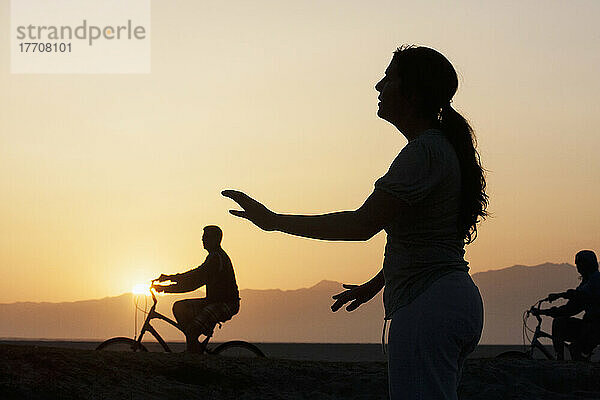 Silhouette von Radfahrern und einer Frau  die bei Sonnenaufgang Yoga macht; Kalifornien  Vereinigte Staaten von Amerika