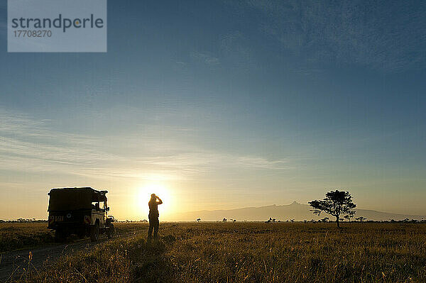 Silhouette einer Frau  die durch ein Fernglas vor dem Berg Kenia in der Morgendämmerung schaut  Ol Pejeta Conservancy; Kenia