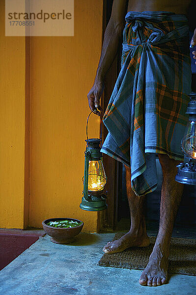 Ein Mann steht in einer Türöffnung und hält beleuchtete Laternen; Ulpotha  Embogama  Sri Lanka