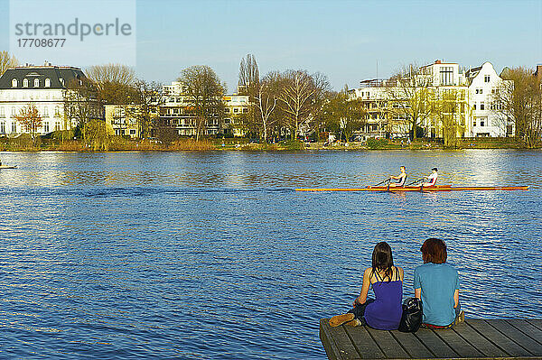 Zwei junge Leute sitzen auf einem hölzernen Dock am Fluss; Hamburg  Deutschland