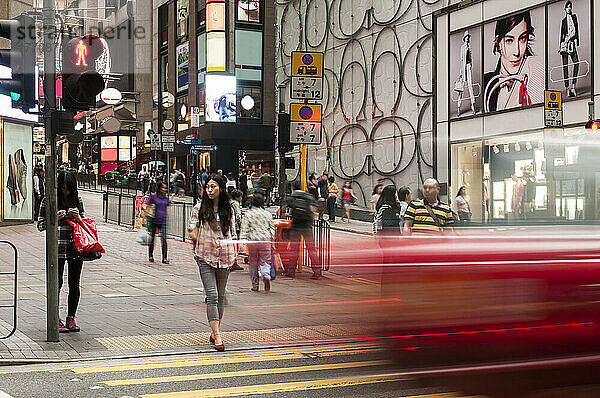 Unschärfe eines Fahrzeugs auf einer Straße  während ein Fußgänger auf die Überquerung wartet; Hongkong  China