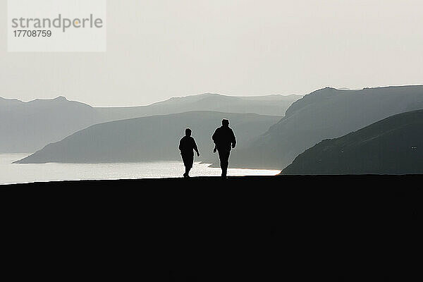 Zwei Wanderer in der Nähe von Martin's Haven bei Sonnenuntergang auf dem Pembrokeshire Coast Path; Wales