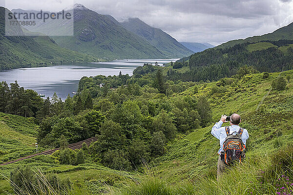 Ein Wanderer macht auf einem Wanderweg eine Pause  um Loch Shiel und die umliegende Landschaft in Glenfinnan  Schottland  zu fotografieren; Glenfinnan  Schottland