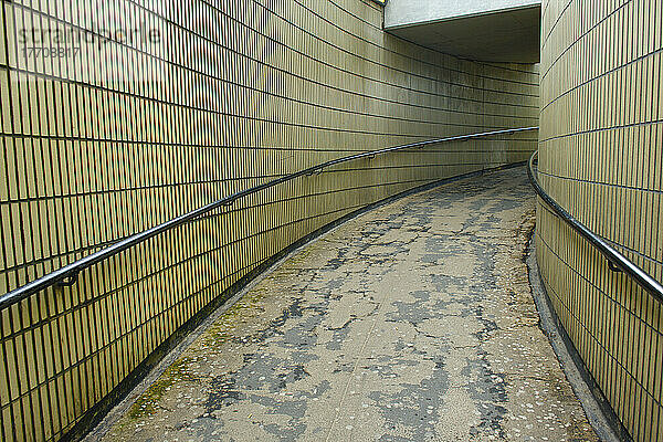 Ein gebogener Gehweg mit Geländer zwischen zwei Backsteinmauern; London  England