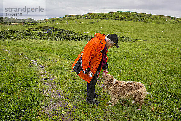 Ein Wanderer hält inne  um einen Hund auf der Isle of Eigg  Schottland  zu streicheln; Isle of Eigg  Schottland