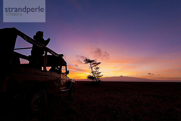 Silhouette eines Touristen und eines Reiseführers in einem Geländewagen vor dem Berg Kenia in der Morgendämmerung  Ol Pejeta Conservancy; Kenia