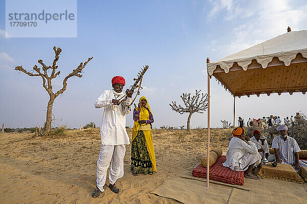 Rajput-Mann  der Ravanahatha spielt  und eine Sängerin  die auf einem Festival mit Dorfältesten auftritt  die in der Wüste Thar in Rajasthan  Indien  eine Wasserpfeife rauchen; Nagaur  Rajasthan  Indien